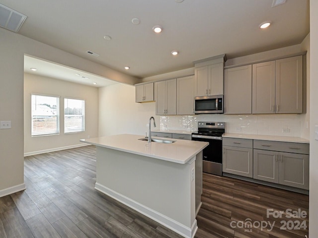 kitchen with gray cabinetry, stainless steel appliances, a center island with sink, dark hardwood / wood-style floors, and sink