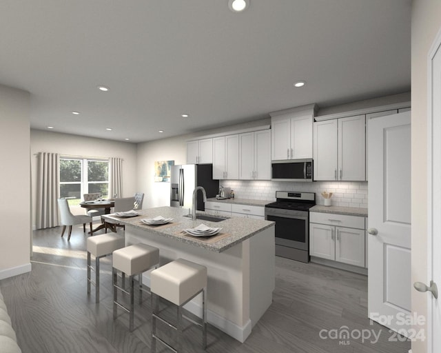 kitchen featuring a kitchen island with sink, white cabinetry, hardwood / wood-style flooring, stainless steel appliances, and a kitchen bar