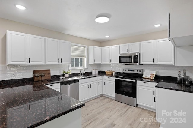 kitchen featuring dark stone countertops, white cabinets, stainless steel appliances, light hardwood / wood-style flooring, and sink