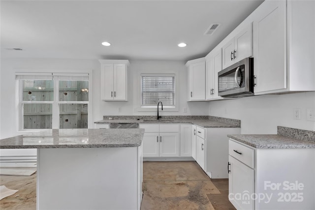 kitchen featuring light stone counters, sink, a kitchen island, and white cabinets