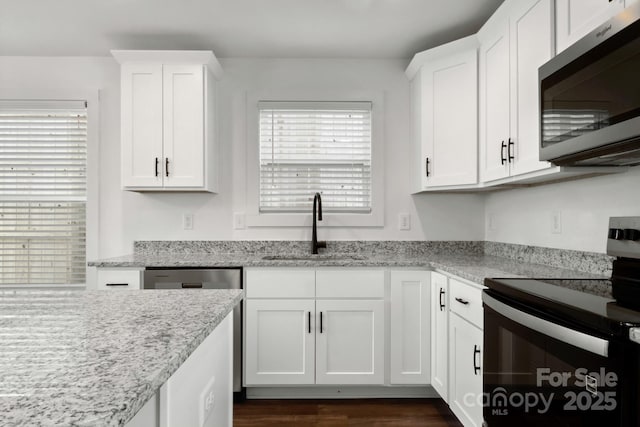 kitchen with stainless steel appliances, white cabinetry, sink, and light stone counters