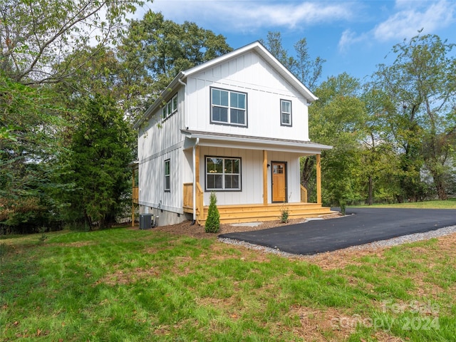 modern farmhouse style home with cooling unit, a front lawn, and covered porch