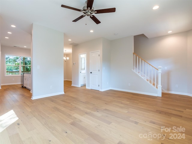 unfurnished living room with ceiling fan with notable chandelier and light hardwood / wood-style floors