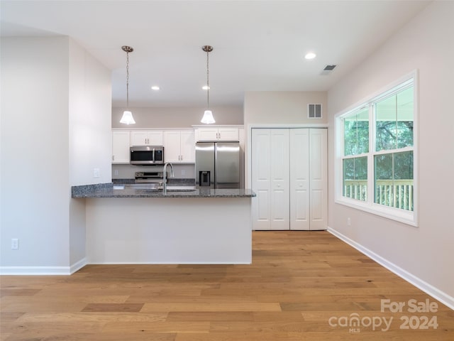 kitchen with white cabinets, stainless steel appliances, pendant lighting, and light hardwood / wood-style floors