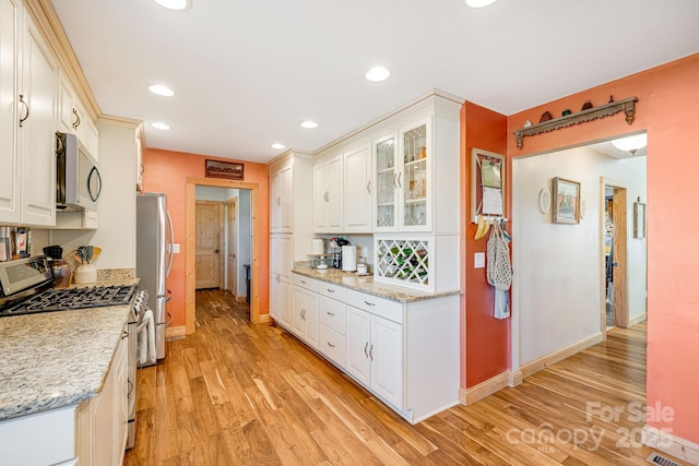 kitchen featuring white cabinetry, appliances with stainless steel finishes, light wood-type flooring, and light stone counters