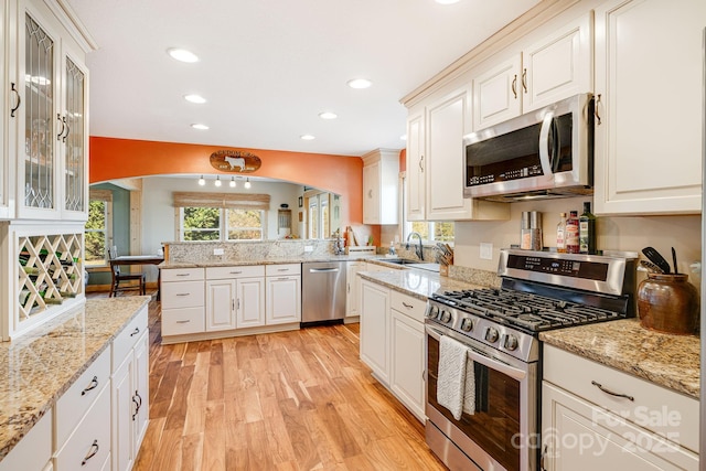 kitchen with stainless steel appliances, white cabinetry, light stone countertops, and light hardwood / wood-style floors