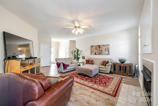 living room featuring a tiled fireplace, light wood-type flooring, and ceiling fan