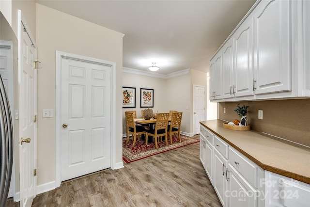 kitchen with ornamental molding, light hardwood / wood-style flooring, stainless steel refrigerator, and white cabinets