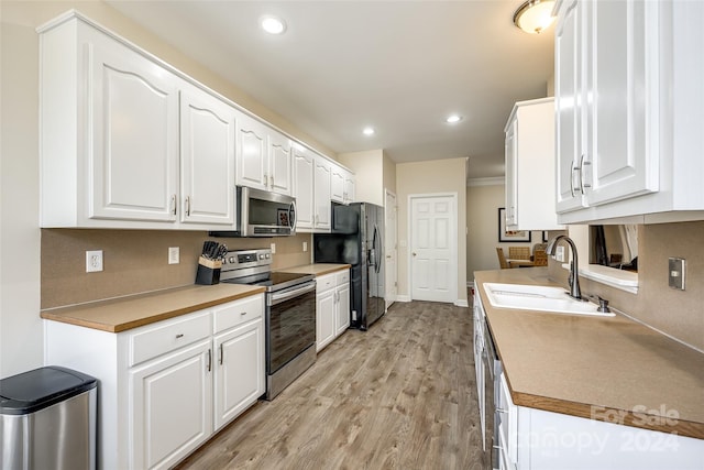 kitchen with sink, white cabinets, light hardwood / wood-style flooring, and stainless steel appliances