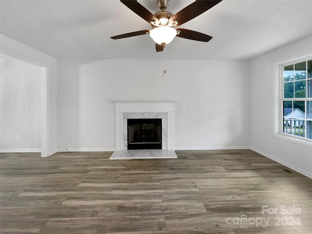 unfurnished living room featuring dark wood-type flooring, ceiling fan, and a premium fireplace