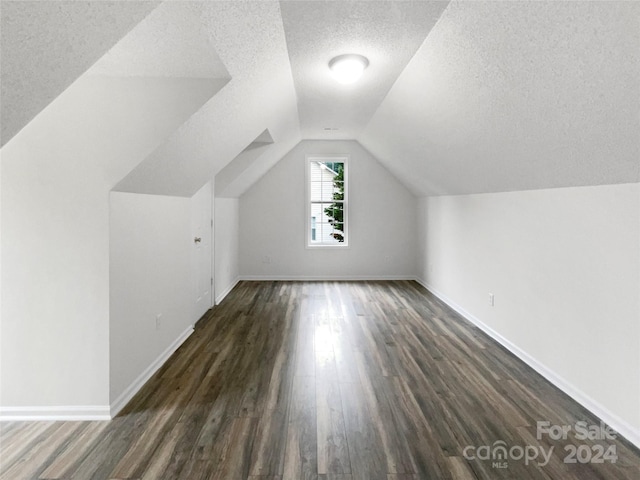 additional living space with a textured ceiling, vaulted ceiling, and dark hardwood / wood-style floors