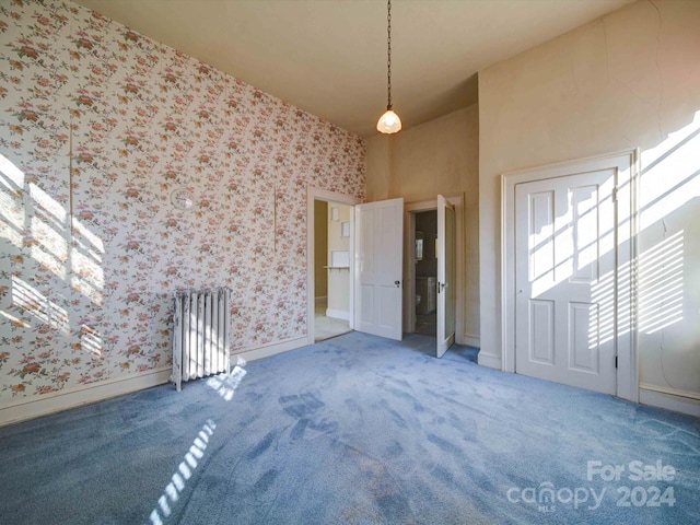 unfurnished room featuring a towering ceiling, radiator heating unit, and carpet flooring