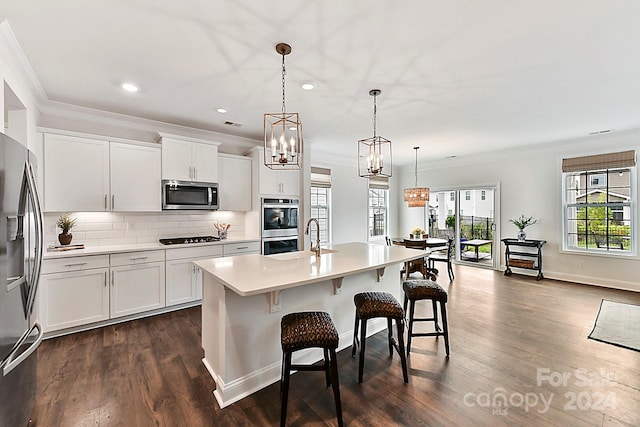 kitchen featuring appliances with stainless steel finishes, white cabinetry, dark hardwood / wood-style flooring, pendant lighting, and a center island with sink