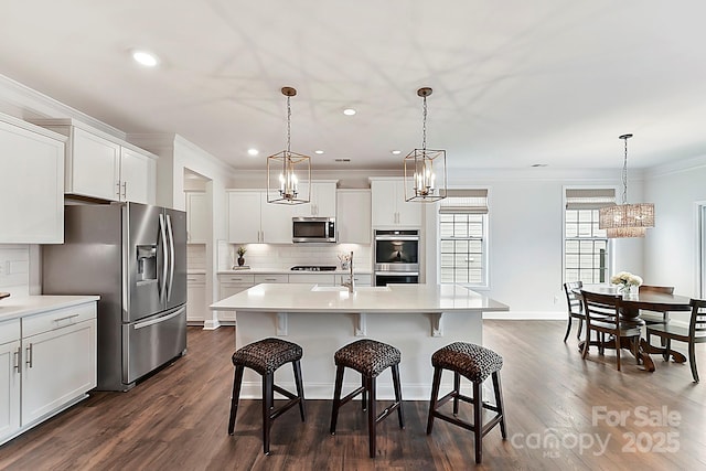 kitchen featuring hanging light fixtures, a center island with sink, stainless steel appliances, and light countertops