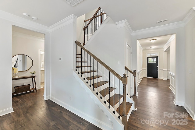 foyer entrance with ornamental molding, wainscoting, visible vents, and dark wood finished floors