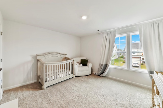 bedroom featuring a nursery area, baseboards, and light colored carpet