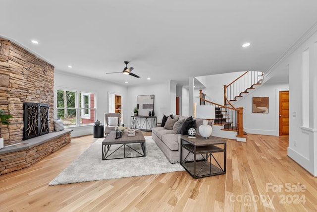 living room featuring ceiling fan, a fireplace, crown molding, and light hardwood / wood-style flooring