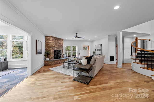 living room with light wood-type flooring, ceiling fan, crown molding, and a stone fireplace