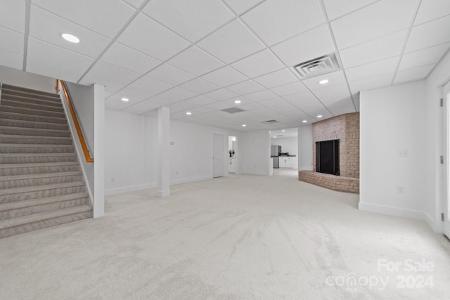 basement featuring a paneled ceiling, stainless steel refrigerator, light carpet, and a brick fireplace