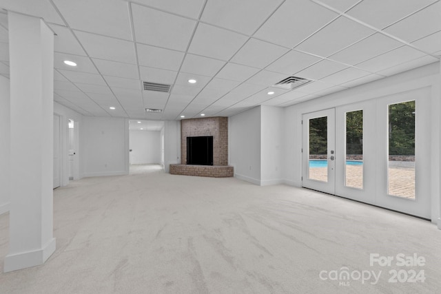 unfurnished living room with light carpet, a brick fireplace, a drop ceiling, and french doors