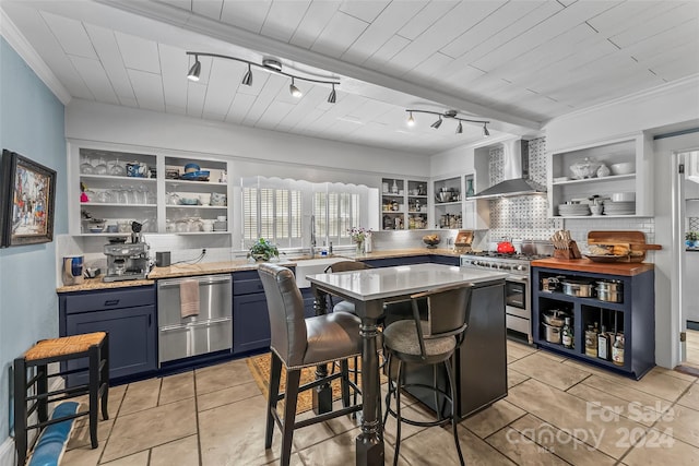 kitchen featuring a breakfast bar area, wall chimney range hood, appliances with stainless steel finishes, light tile patterned floors, and blue cabinetry