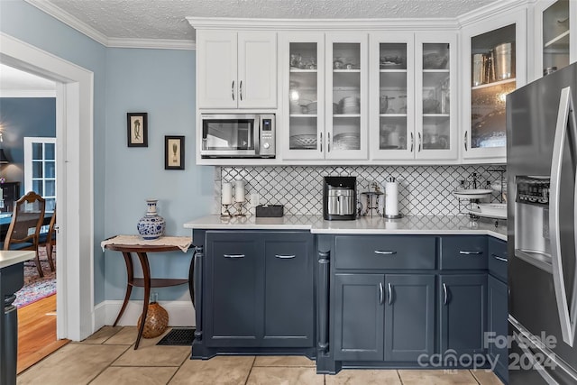 bar with light tile patterned flooring, white cabinets, appliances with stainless steel finishes, ornamental molding, and blue cabinetry