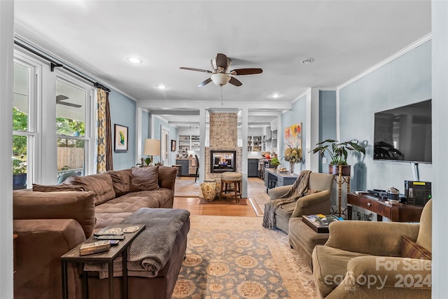 living room with ceiling fan, a stone fireplace, crown molding, and hardwood / wood-style floors