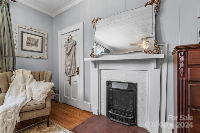 living room with crown molding, wooden walls, ceiling fan, and a brick fireplace