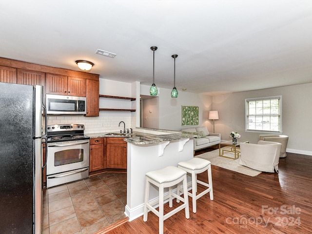 kitchen with a breakfast bar, sink, stainless steel appliances, decorative light fixtures, and light stone countertops