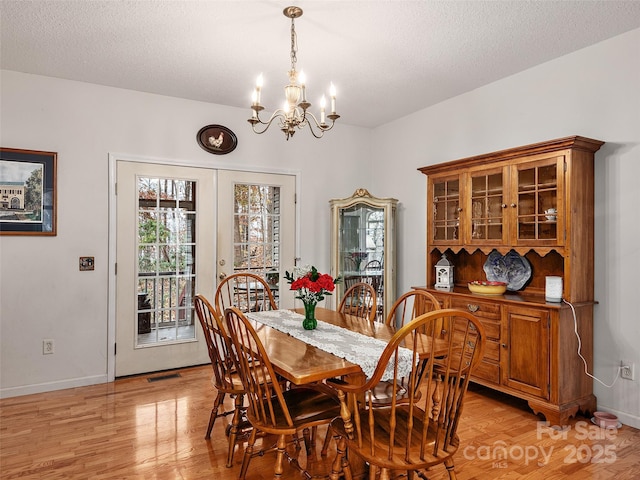 dining area with french doors, a textured ceiling, light hardwood / wood-style floors, and an inviting chandelier