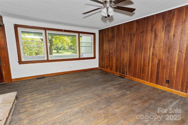 empty room featuring ceiling fan, dark hardwood / wood-style floors, crown molding, and wooden walls