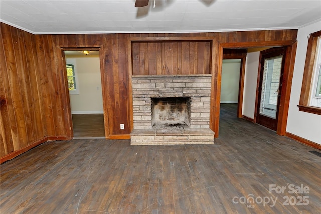 unfurnished living room featuring wood walls, dark hardwood / wood-style flooring, crown molding, and a stone fireplace