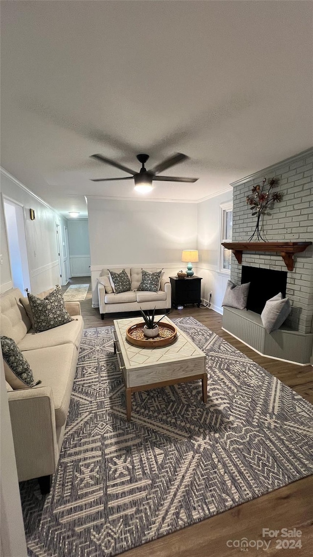 living room with a textured ceiling, hardwood / wood-style flooring, a fireplace, ornamental molding, and ceiling fan