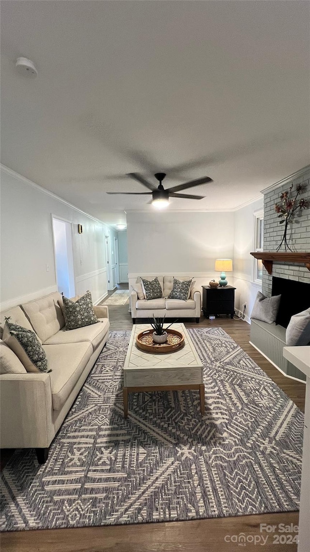 living room featuring a brick fireplace, hardwood / wood-style flooring, ornamental molding, and ceiling fan