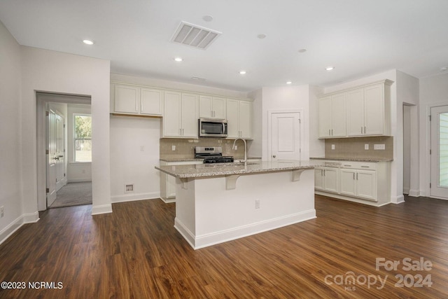 kitchen with a center island with sink, dark wood-type flooring, stainless steel appliances, a kitchen breakfast bar, and light stone countertops