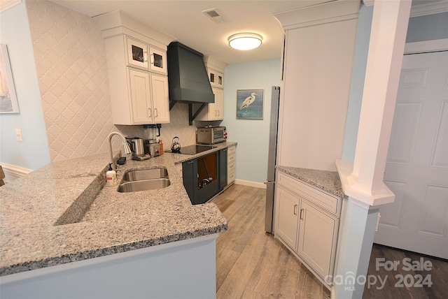 kitchen featuring kitchen peninsula, light stone countertops, light hardwood / wood-style flooring, premium range hood, and sink