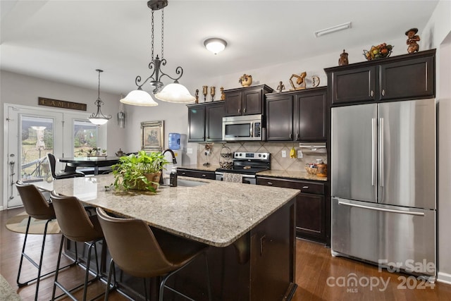 kitchen featuring sink, decorative light fixtures, a center island with sink, stainless steel appliances, and dark hardwood / wood-style floors