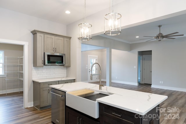 kitchen with ceiling fan, hanging light fixtures, a kitchen island with sink, appliances with stainless steel finishes, and light stone countertops