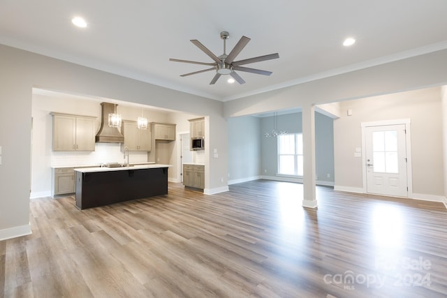 unfurnished living room with light wood-type flooring, ceiling fan with notable chandelier, crown molding, and sink