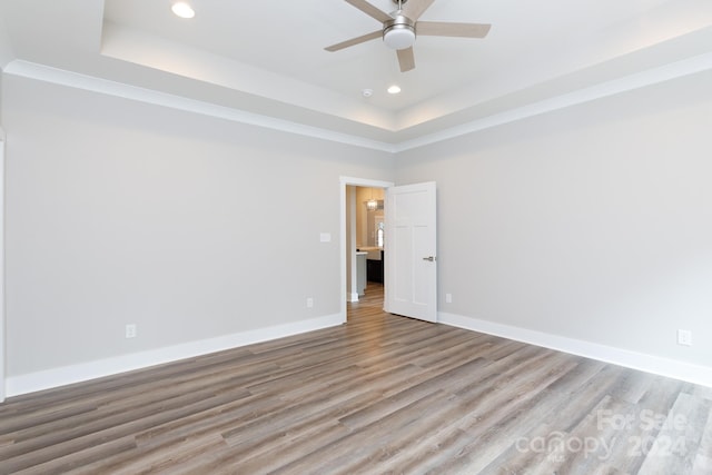 spare room with ceiling fan, a tray ceiling, and light hardwood / wood-style floors