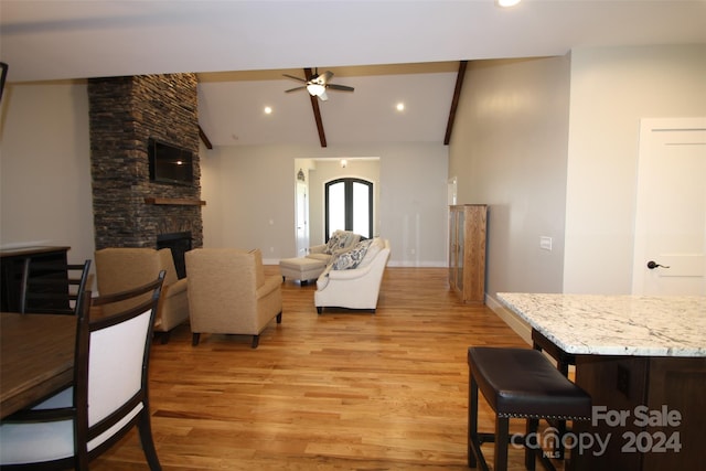 living room featuring ceiling fan, vaulted ceiling, a stone fireplace, and light hardwood / wood-style floors