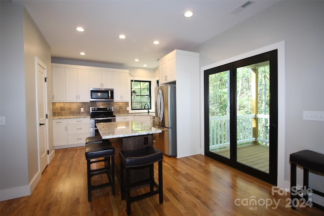 kitchen featuring a kitchen island, light hardwood / wood-style flooring, stainless steel appliances, light stone countertops, and white cabinetry