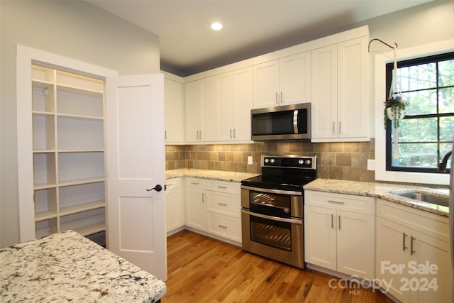 kitchen with light stone counters, white cabinets, stainless steel appliances, and light hardwood / wood-style flooring