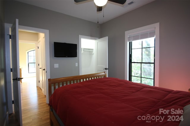 bedroom featuring light hardwood / wood-style floors, a wall unit AC, ceiling fan, a spacious closet, and a closet