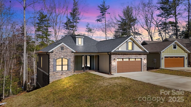 view of front facade with an attached garage, stone siding, driveway, a front lawn, and board and batten siding