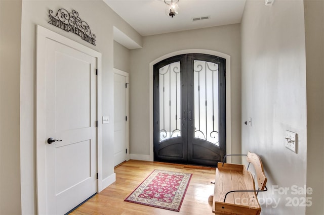 foyer featuring light wood-type flooring, french doors, visible vents, and arched walkways