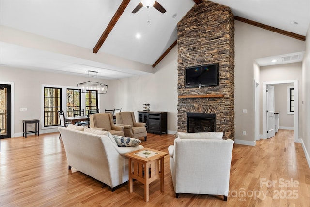 living room with a stone fireplace, ceiling fan with notable chandelier, visible vents, baseboards, and light wood-type flooring