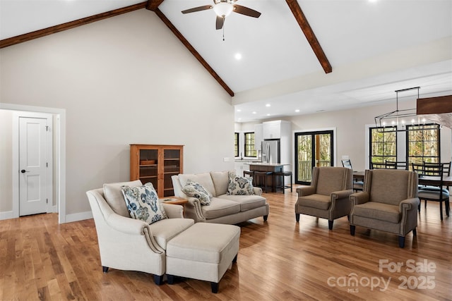 living area featuring baseboards, light wood-style flooring, high vaulted ceiling, beam ceiling, and ceiling fan with notable chandelier