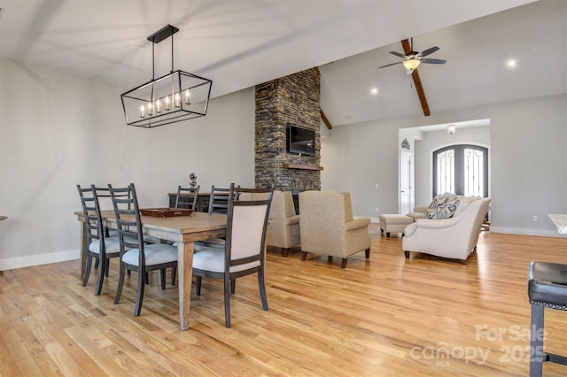 dining room featuring baseboards, ceiling fan, a stone fireplace, light wood-type flooring, and high vaulted ceiling