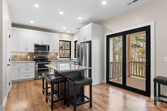 kitchen featuring light stone counters, visible vents, decorative backsplash, appliances with stainless steel finishes, and a kitchen breakfast bar